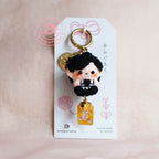 Keychain with a character design on a white card against a pink background