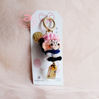 Keychain with plush figure on a white card with brand logo, on a beige background