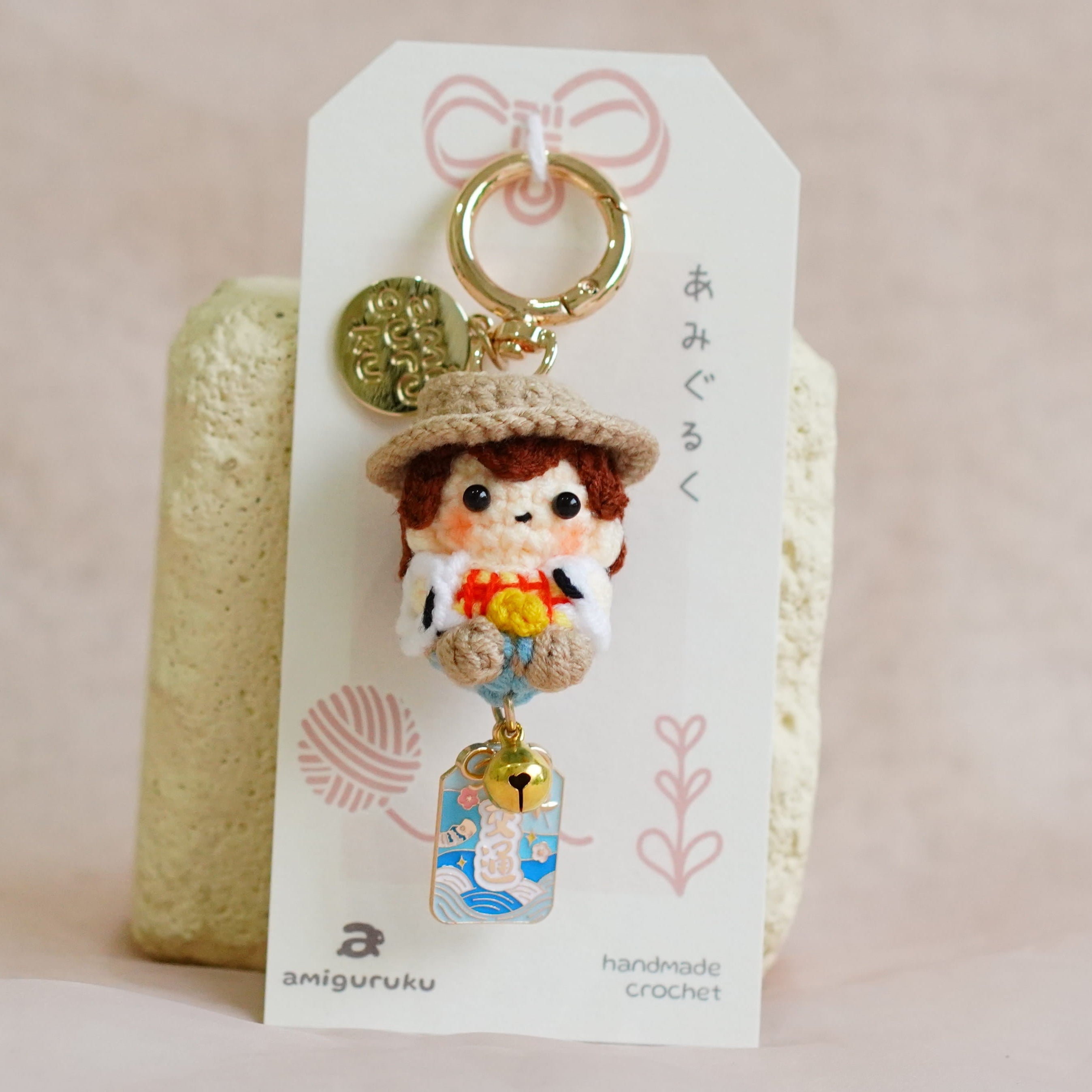 A handmade Japanese doll keychain charm displayed on its white paper packaging card, set against a soft beige fabric background.