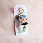 Keychain with a plush character on a white card against a beige background