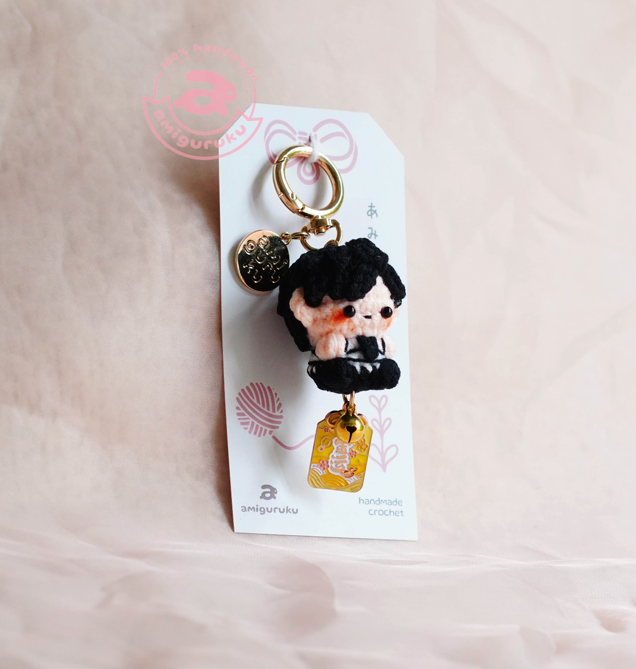 Keychain with a character on a white card with 'amiguruku' branding, on a beige background.